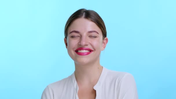 Lively Caucasian woman with vibrant red lips bursts into laughter, joy filling the air against a serene blue backdrop. Infectious laughter is accompanied by a radiant smile. - Footage, Video