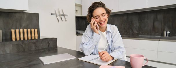 Image d'une femme travaillant à domicile, écrivant des informations lors d'un appel téléphonique, appelant quelqu'un, utilisant un smartphone. - Photo, image