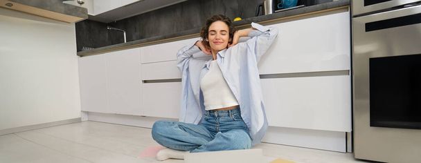 Work from home and lifestyle concept. Happy brunette girl finishes assignment, sits on floor with laptop and homework and stretches her hands with pleased face. - Photo, Image