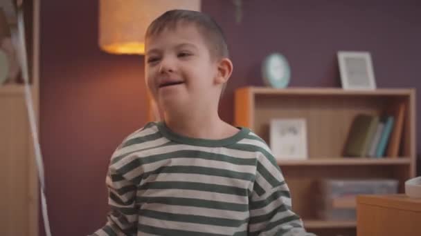 Wesoły biały 6-letni chłopiec z zespołem Downa zabawy podczas zabawy z kolorowe balony w domu - Materiał filmowy, wideo