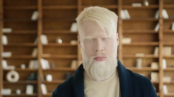 Vakava albiinotyyppi heiluttaa päätään ei virassa. Pensive liikemies eri mieltä päätöksestä. Ajattelevainen yrittäjä nostaa kulmakarvojaan. Utelias mies muotokuva kirjahyllyillä taustalla, 4k kuvamateriaalia - Materiaali, video