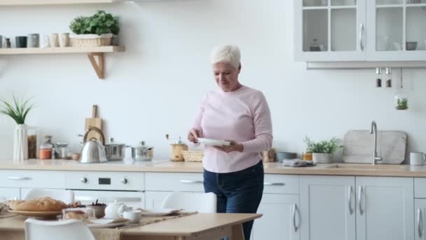 Vaaliminen valkoihoinen nainen järjestää lautaset pöydälle keittiössä. Hänen kätensä liikkuvat tarkoituksella ja lempeästi, varmistaen, että jokainen levy löytää paikkansa tarkasti.. - Materiaali, video