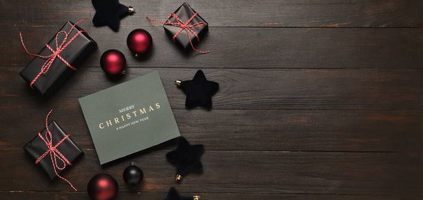 Gyönyörű karácsonyi kompozíció üdvözlőkártyával, ajándékdobozokkal és dekorációkkal fából készült háttérrel, szöveggel - Fotó, kép