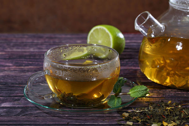 Tea in a glass teapot and a transparent cup with lime and mint o - Photo, Image