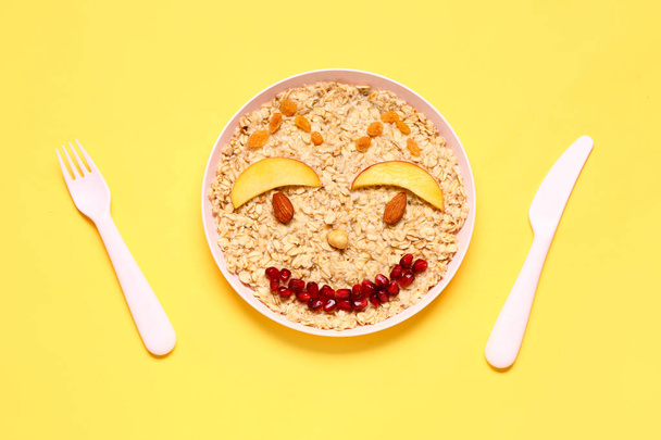 Plate of funny oatmeal for children and cutlery on yellow background - Photo, Image