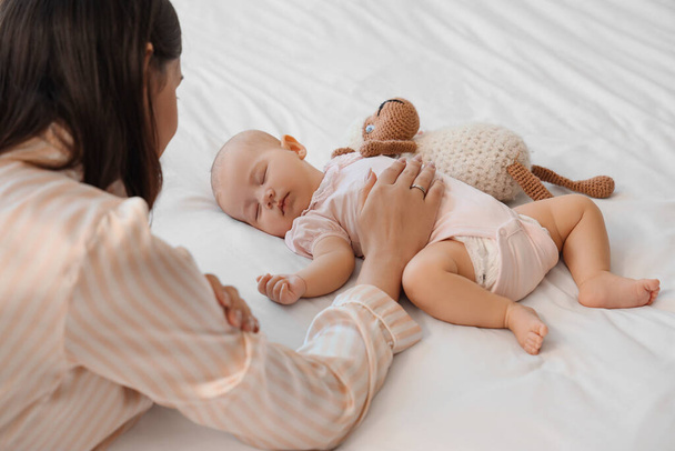 Mother and little cute baby with toy sleeping on bed at home - Photo, Image