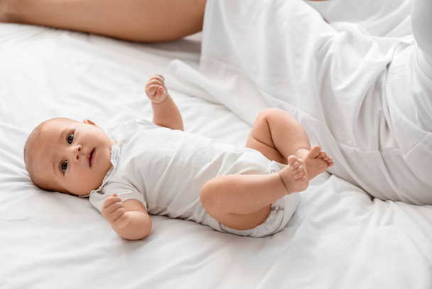 自宅でベッドに横たわるかわいい小さな赤ちゃんと幸せな母親 - 写真・画像
