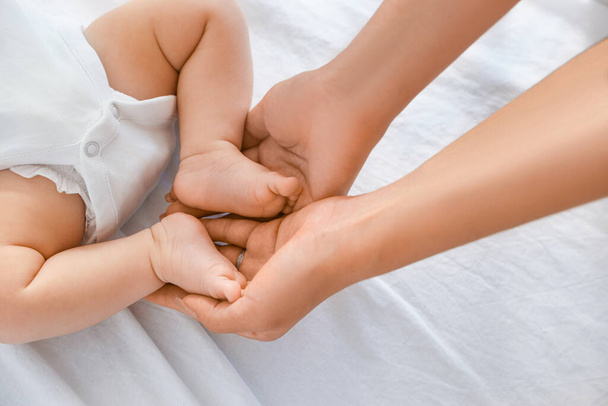 Τα χέρια της μητέρας με μικροσκοπικά πόδια μωρού στην κούνια στο σπίτι - Φωτογραφία, εικόνα