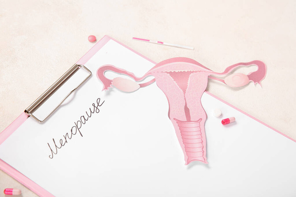 Klembord met woord MENOPAUSE, pillen, papieren baarmoeder en zwangerschapstest op lichte achtergrond, close-up - Foto, afbeelding