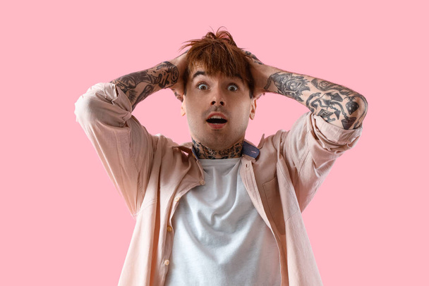 Asustado joven hombre tatuado sobre fondo rosa - Foto, Imagen
