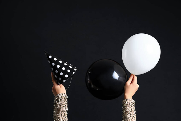 Manos femeninas con cono de fiesta y globos sobre fondo negro - Foto, imagen