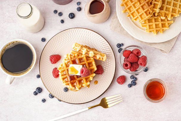 Вкусные вафли с ягодами, кленовый сироп, молоко и чашка кофе на белом фоне - Фото, изображение