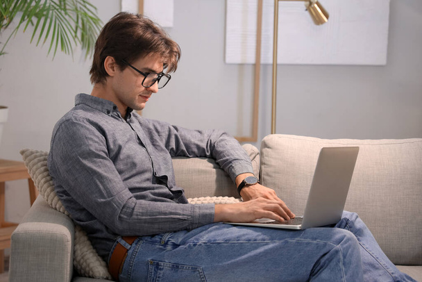 Joven hombre de negocios sentado en el sofá en la oficina y trabajando con el ordenador portátil - Foto, imagen