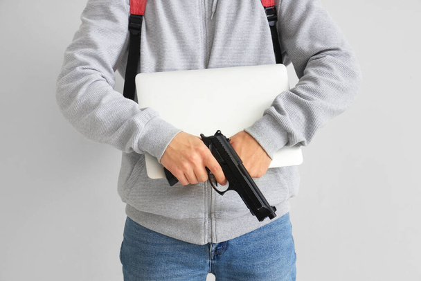 Studente di sesso maschile con pistola e portatile su sfondo chiaro, primo piano. Scuola tiro concetto - Foto, immagini