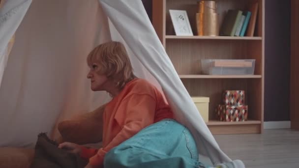 Caucasian blond haired woman and her little son with down syndrome playing and resting in cozy tent in living room - Footage, Video