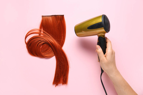 Mano femenina con secador y cabello de jengibre sobre fondo rosa - Foto, Imagen