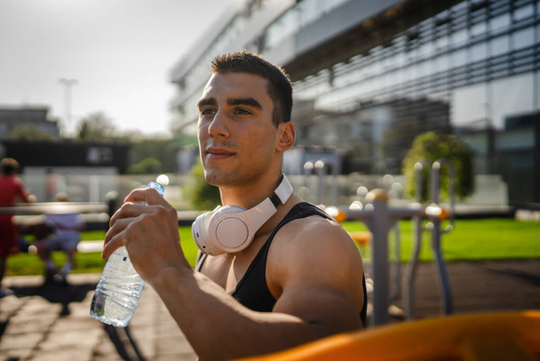 een man Kaukasische mannelijke atleet houden plastic fles water openen en voor te bereiden om te drinken tijdens de training buiten in zonnige dag hydratatie en gezonde levensstijl concept kopiëren ruimte - Foto, afbeelding