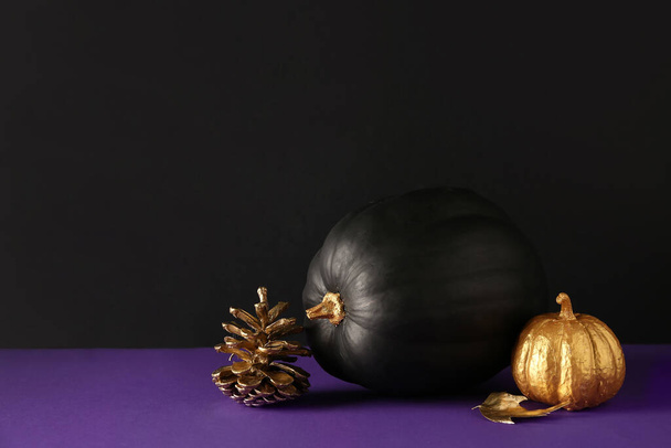 Bemalte Kürbisse mit goldenem Kegel und Blatt auf violettem Tisch neben schwarzer Wand - Foto, Bild