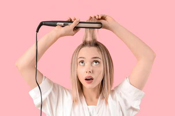 Шокированная молодая блондинка выпрямляет волосы на розовом фоне - Фото, изображение