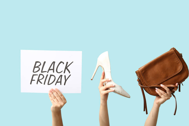 Female hands holding poster with text BLACK FRIDAY and women accessories on blue background - Foto, afbeelding