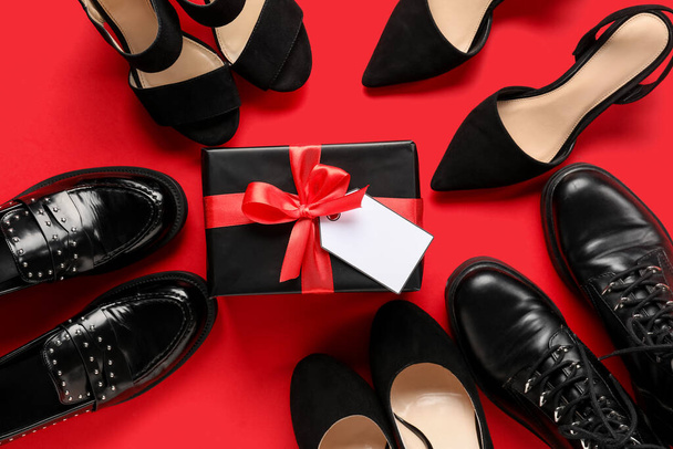 Joukko erilaisia naisten kengät ja lahja laatikko tyhjä tag punaisella taustalla. Musta perjantai myynti - Valokuva, kuva