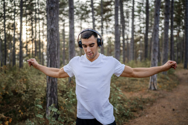 een man jonge Kaukasische mannelijke atleet stretch in het bos in de natuur outdoor joggen of oefenen in de herfst of de zomer dag sport fitness en recreatie gezonde levensstijl concept echte mensen kopiëren ruimte - Foto, afbeelding