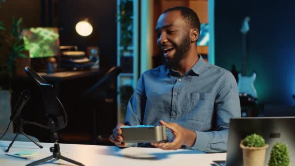 African american internet star doing technology review of Bluetooth portable speaker for online platforms channel. BIPOC influencer presenting music playing device to his viewership - Footage, Video