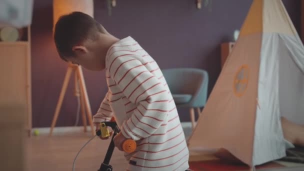 Petit garçon avec le syndrome du duvet essayant de faire du vélo dans un salon spacieux - Séquence, vidéo