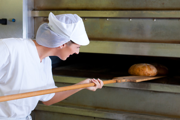 Female baker baking fresh bread in the bakehouse - Photo, Image