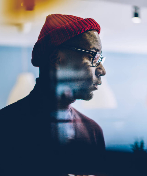 Serious african american hipster guy in spectacles looking at window pondering on ideas in office, young dreamy dark skinned businessman in casual wear and hat concentrated on planning - 写真・画像