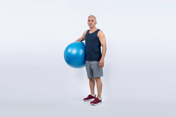 Koko kehon pituus laukaus urheilullinen ja urheilullinen vanhempi mies kunto käyttäessään palloa seisovan ryhti eristetty tausta. Terveet aktiiviset ja kehonhoitotavat eläkkeelle siirtymisen jälkeen. Vaikutusvalta - Valokuva, kuva