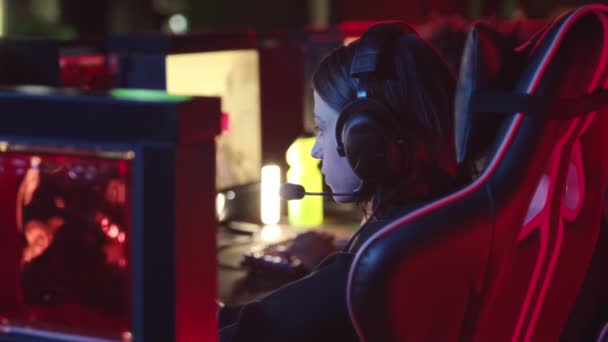 Waist up slowmo portrait of Caucasian gamer girl looking seriously at camera while playing first person shooter game on PC in dark esports club - Footage, Video