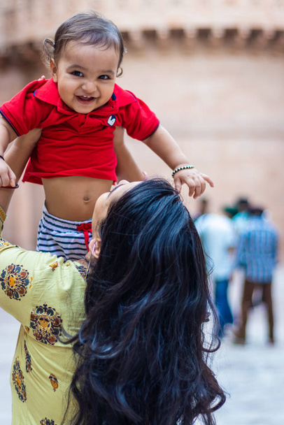 χαριτωμένο μικρό παιδί αγόρι χαμογελά στο χέρι της μητέρας και να αγγίξει σε casual εμφάνιση σε υπαίθριο - Φωτογραφία, εικόνα