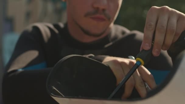 Közepes közelkép fiatal kaukázusi kerekesszékes férfi használ csavarhúzó, miközben javítás az adaptív supboard szabadban - Felvétel, videó