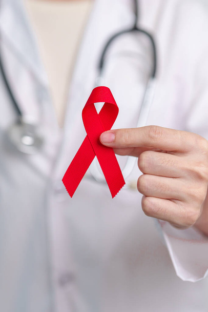 Arzt mit rotem Band zum Welt-Aids-Tag im Dezember, erworbenes Immunschwächesyndrom, Monat des Bewusstseins für Multiples Myelom Krebs und Nationale Woche der roten Schleife. Konzept zum Gesundheits- und Weltkrebstag - Foto, Bild