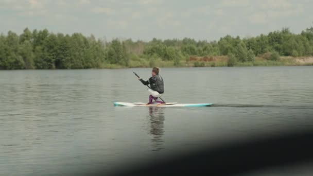 Panning shot van Kaukasische tiener jongen zonder benen sup surfen met peddel op adaptieve sup board buiten in de zomer - Video