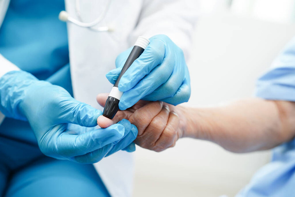 Lekarz azjatycki używający wstrzykiwacza lancetowego na palcu starszego pacjenta w celu sprawdzenia stężenia cukru we krwi w leczeniu cukrzycy. - Zdjęcie, obraz