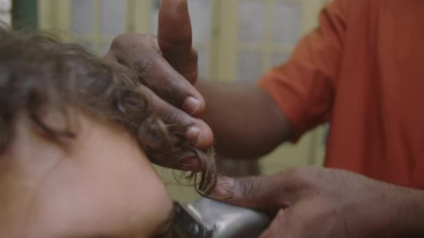 Τραβηγμένο πλάνο των χεριών του μαύρου κουρέα χρησιμοποιώντας χορτοκοπτικό, ενώ κάνει κούρεμα για σγουρά μαλλιά αρσενικό πελάτη στο κουρείο - Πλάνα, βίντεο