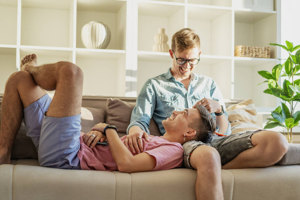 Young happy cute gay couple spending time in a modern apartment talking on the sofa. LGBT family concept - Photo, image