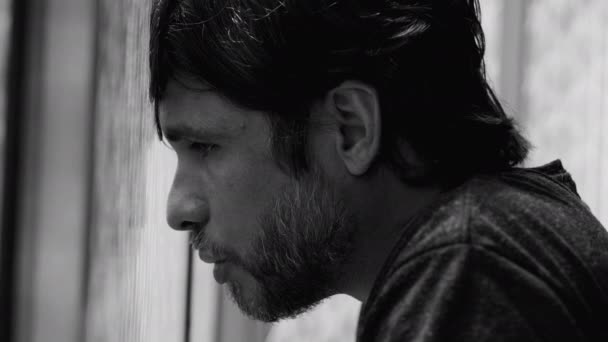 Profile face closeup of a depressed young man leaning on window suffering alone from mental distress. Male person in despair and regret in monochromatic black and white - Footage, Video