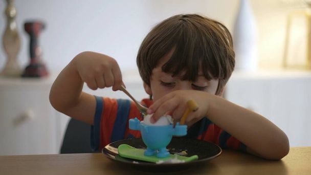 Один маленький хлопчик, що їсть м'яке варене яйце, робить коктейль ла. Дитина їсть легку їжу сам з ложкою - Фото, зображення