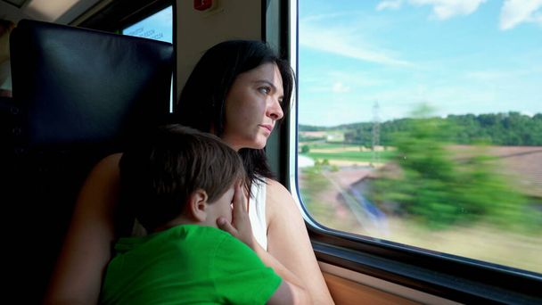 Bedachtzame moeder op snelle Europese trein, omhelzing van haar kind, staren naar het vluchtige platteland - Foto, afbeelding