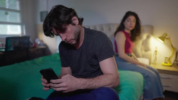 Pareja desconectada: Novio mirando el teléfono ignorando a su novia en el dormitorio. Hombre no comunicativo absorbido por las redes sociales en línea, mientras que la mujer quiere atención - Metraje, vídeo