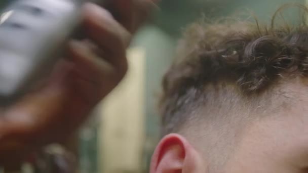 Close up tiro de mão de barbeiro masculino aparar templos de cliente com cortadores de cabelo ao fazer corte de cabelo no salão - Filmagem, Vídeo