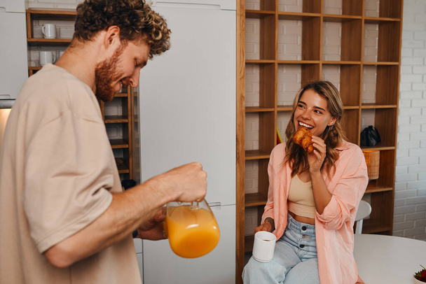 A young married couple in love having breakfast in the morning in the kitchen in a cozy home on their day off while romantically spending time together. - Foto, immagini