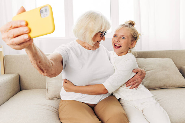 笑顔のビデオ電話コール 人々 スペースを接続する教育白Tシャツの子供 2 つの祖母のセルフィーのコピー ソファーの孫娘の家族 - 写真・画像
