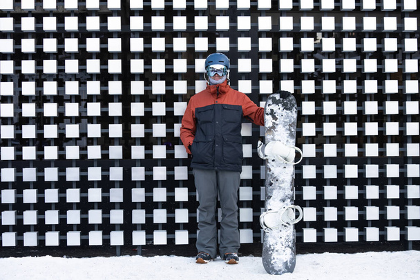 Portrait of a man with snowboard on the background of a fence. Man with snowboard in winter dolomites, alps. - Photo, Image