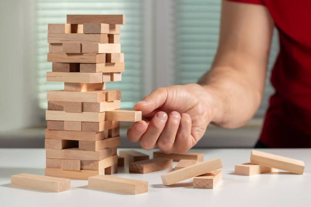 The tower from wooden blocks and man's hand take one block. - Photo, Image