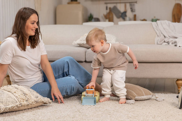 Happy family at home. Mother and baby boy playing with toys at home indoors. Little toddler child and babysitter nanny having fun together. Young woman mom kid son rest in living room - Photo, Image