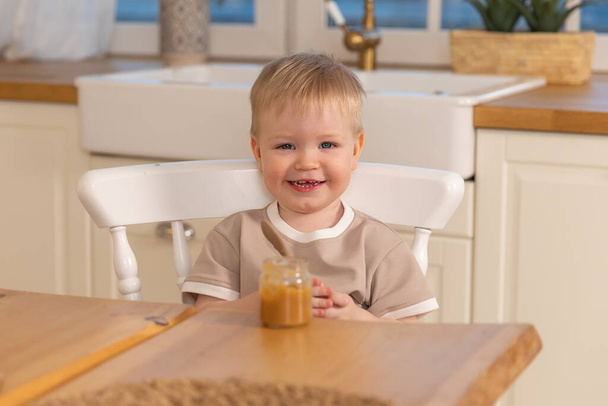 家庭で幸せな家族。子供が台所で食事をしている。乱雑な面白い顔をした小さな男の子は健康的な食べ物を食べる。子供はスプーンを持って一人で食べる。自給自足 - 写真・画像